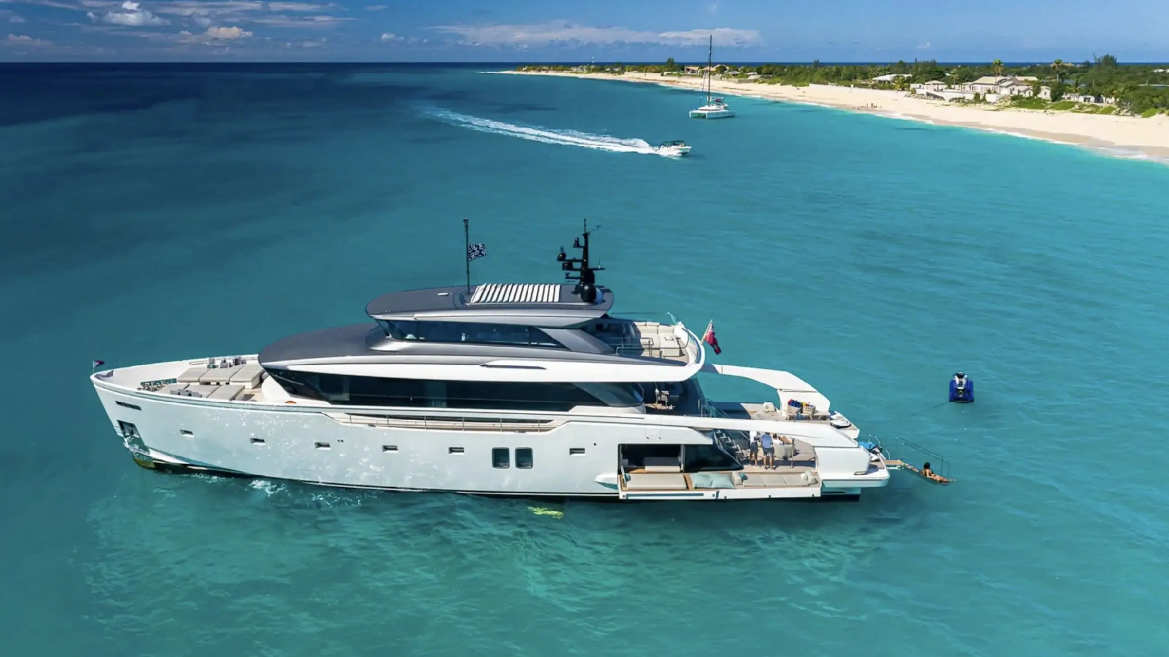 Large yacht on blue water near a sandy shoreline under clear sky.