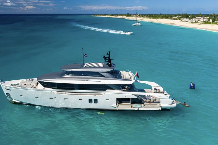Large yacht on blue water near a sandy shoreline under clear sky.