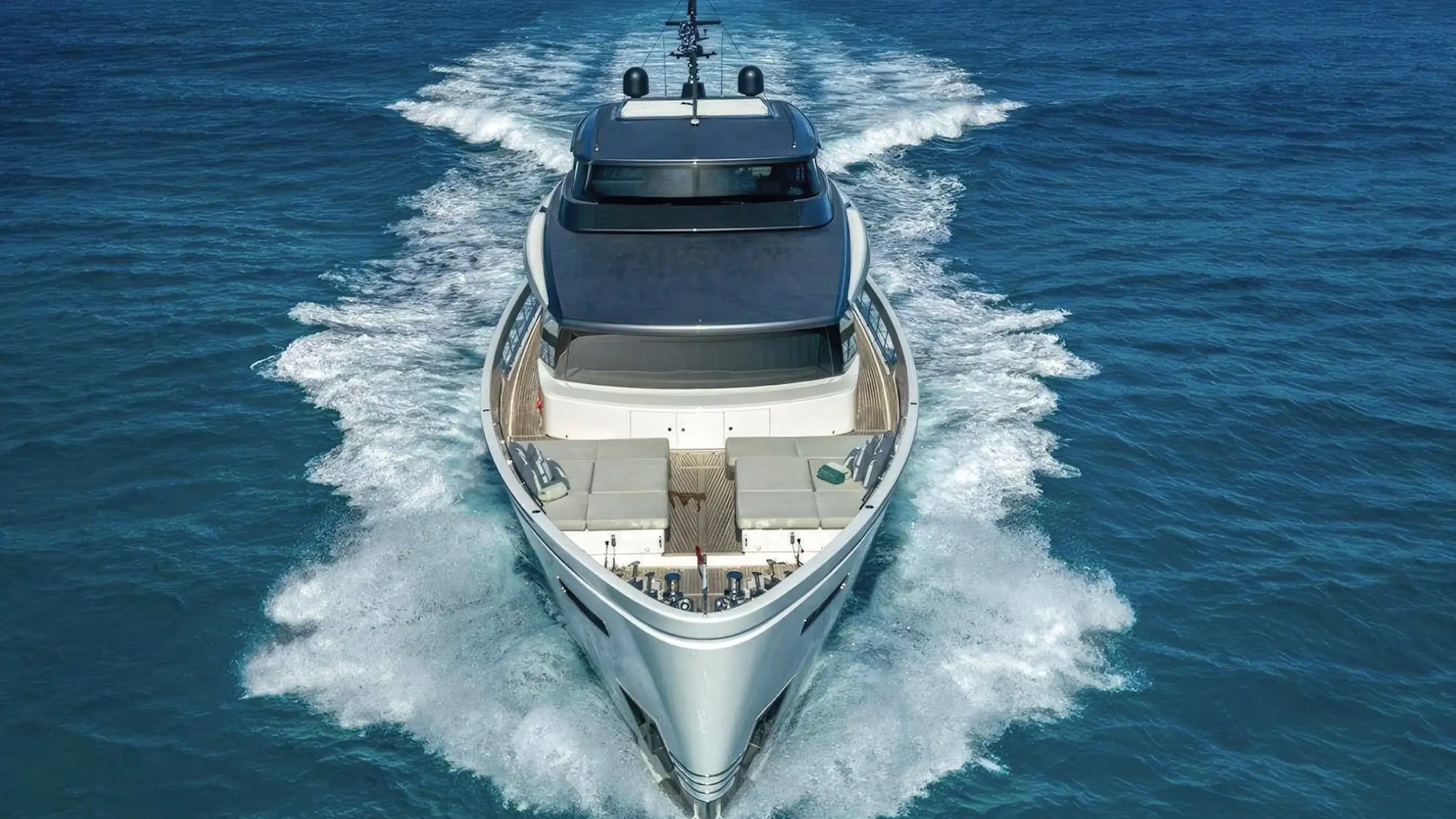 Luxury yacht cruising on open sea, leaving a trail of waves behind.