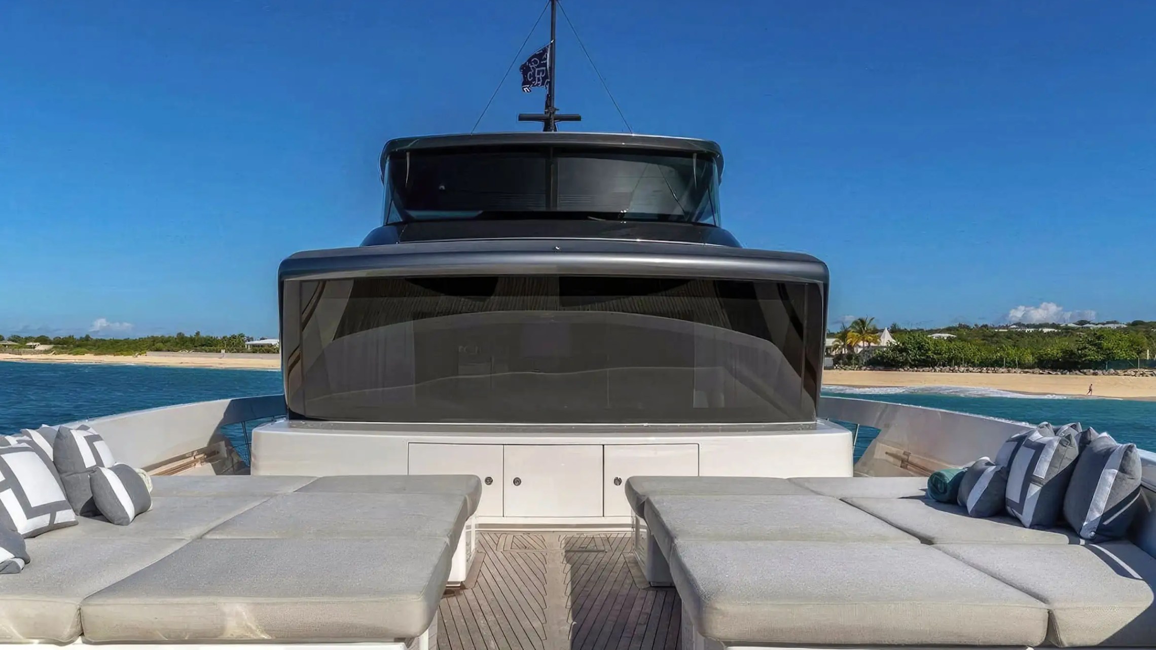View from a yacht's deck towards a beach, with cushions and clear blue sky.