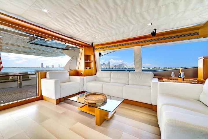Luxurious yacht interior with white sofas, glass table, and ocean view through large windows.