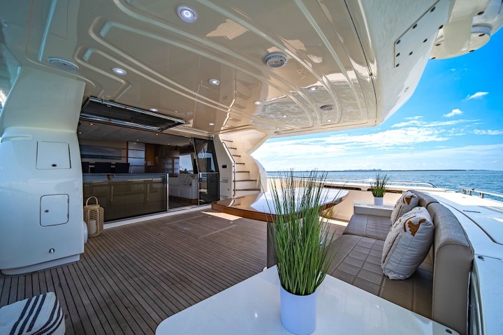 Luxurious yacht deck with seating, table, plants, ocean view, and open interior space.