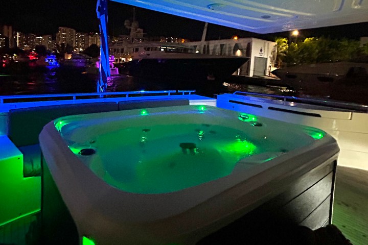 Outdoor hot tub on a boat deck, illuminated with green and blue lights at night, city in the background.