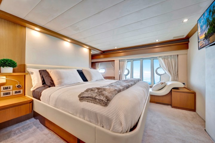 Luxury yacht bedroom with large bed, TV, porthole windows, and elegant decor.