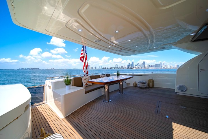 Luxury yacht deck with seating, table, and city skyline view, featuring a flag and potted plants.