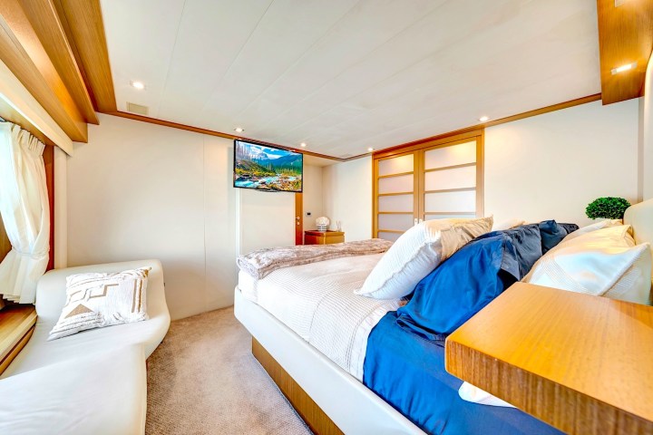 Modern bedroom with a bed, TV, sofa, and sliding wooden doors, featuring soft lighting and neutral tones.