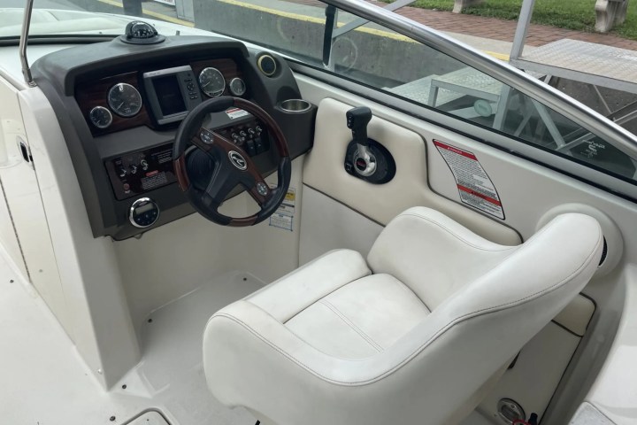 Boat cockpit with steering wheel, controls, and a white captain's chair.