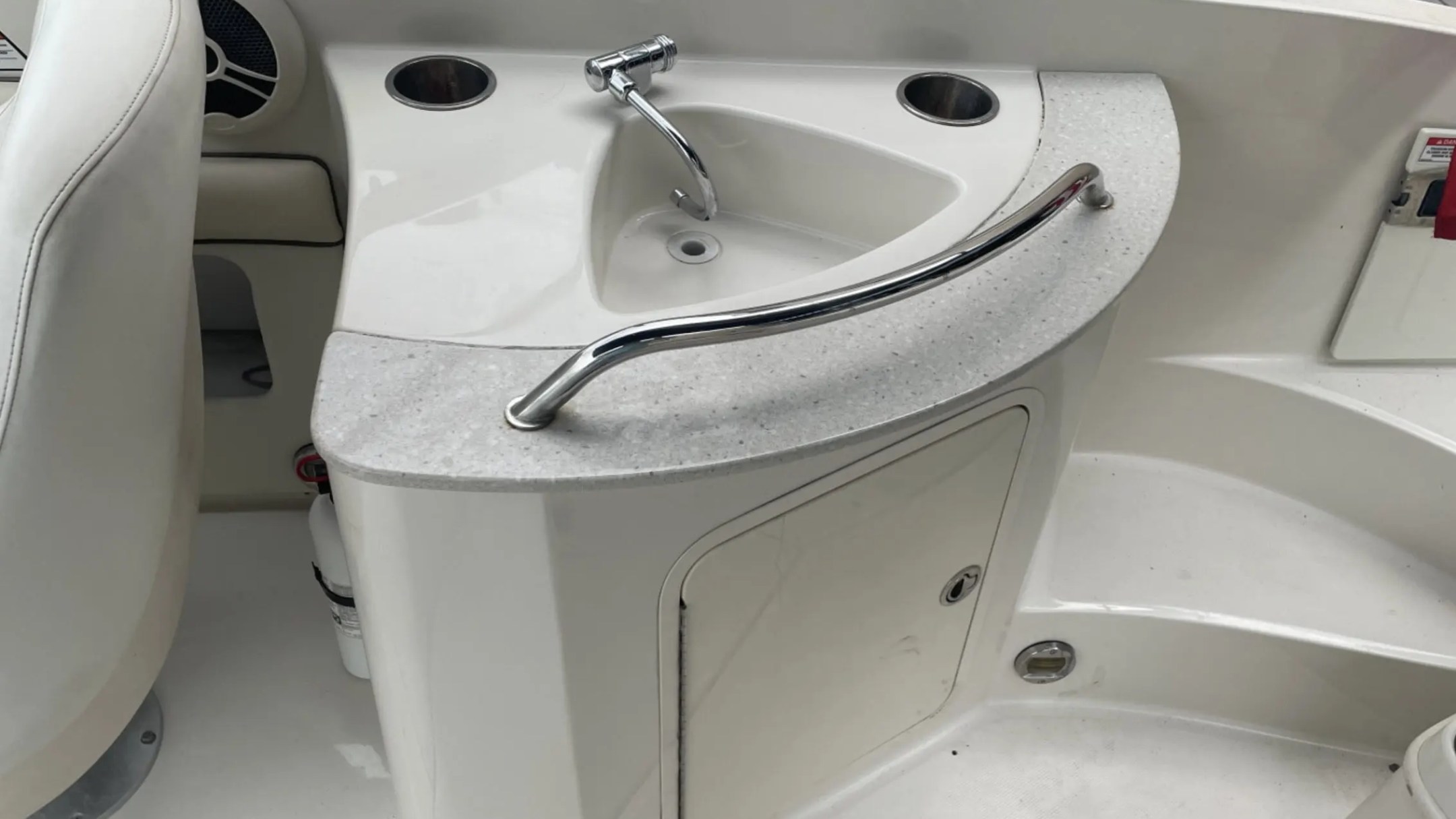 Boat interior with a small sink, faucet, and storage cabinet.