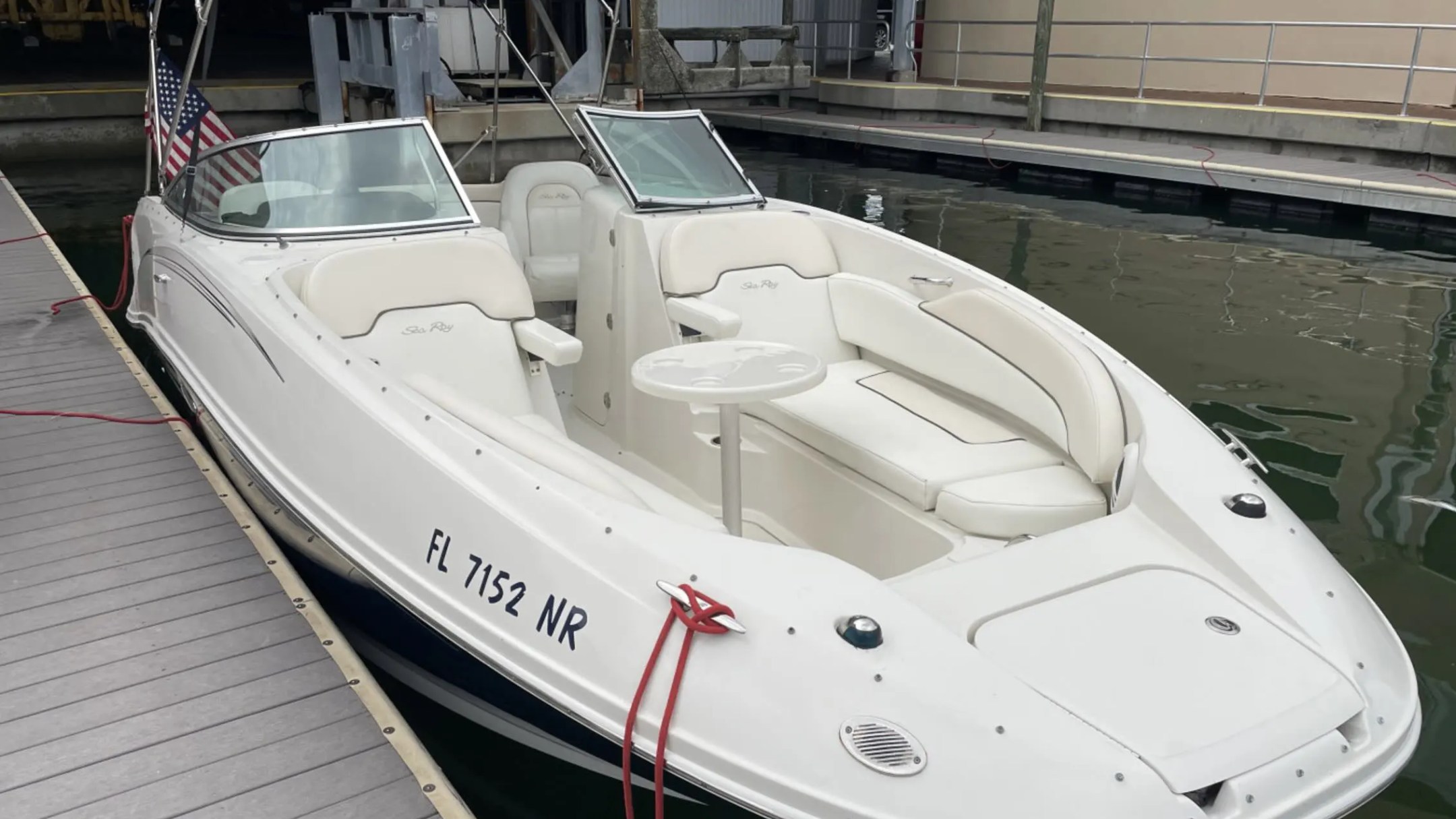 White motorboat with canopy docked, showing seats and table, with American flag at stern.