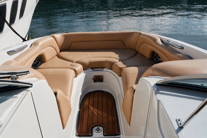 Boat interior with beige seats and wooden floor, beside water.