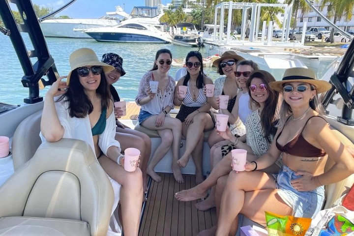 Eight women on a boat holding pink cups, smiling at the camera.