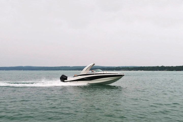Speedboat moving fast on a lake with a cloudy sky and distant treeline.