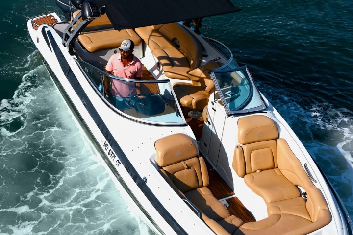 Man steering a white motorboat with beige seats on blue water.