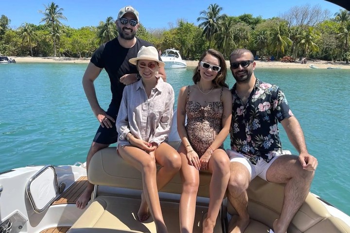 Four people smiling on a boat with tropical trees and clear water in the background.