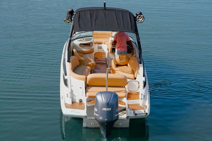 Man steering a brown leather-seated motorboat on calm water, rear view.