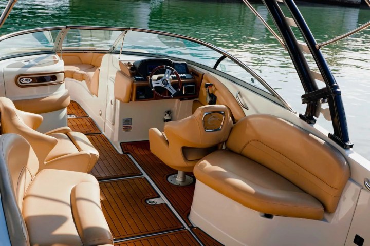 Luxurious boat interior with tan leather seats and wooden flooring, overlooking calm water.