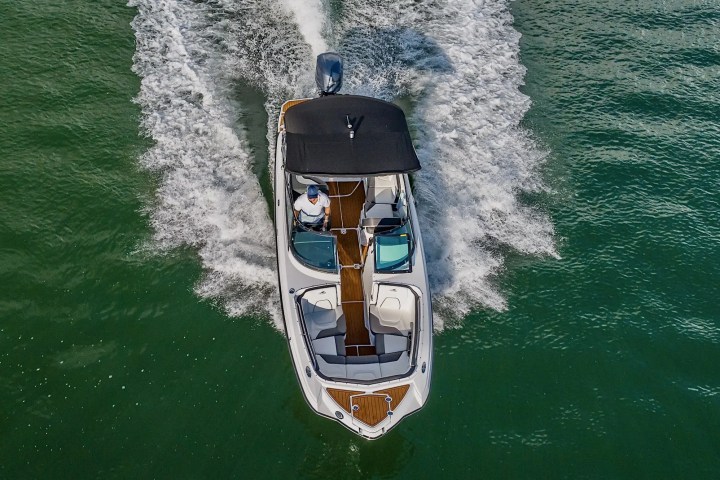Top view of a motorboat with a canopy speeding on green water.