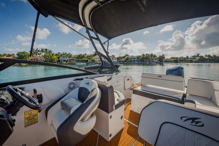 Interior of a motorboat with white seating, steering wheel, and lake view with cloudy sky.