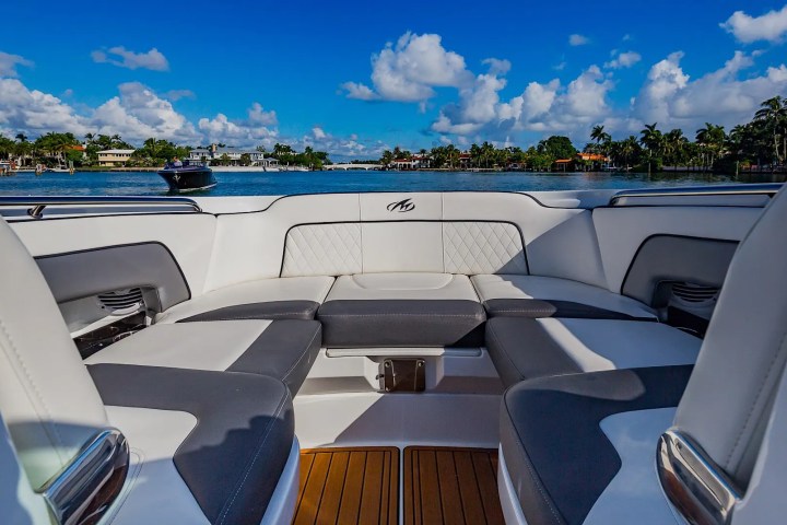 Boat interior with white and gray seating, view of water and palm trees.