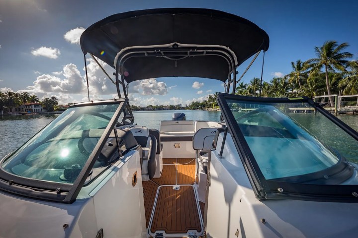 Front view of a boat with a canopy top, on a sunny day with palm trees and clouds.