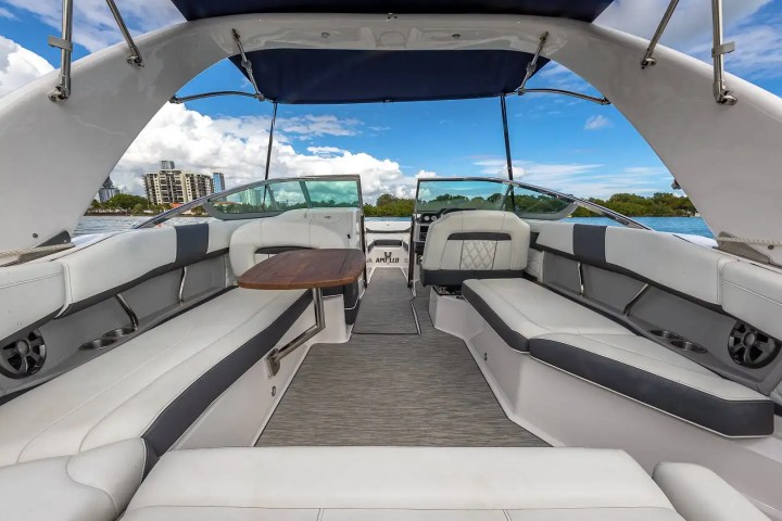 Luxurious boat interior with white cushioned seating and a wooden table under a sunny sky.