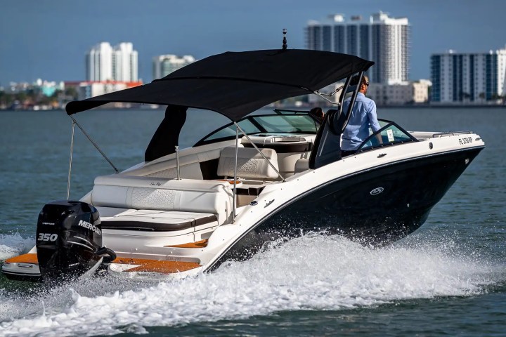Speedboat with canopy on water, cityscape in background.