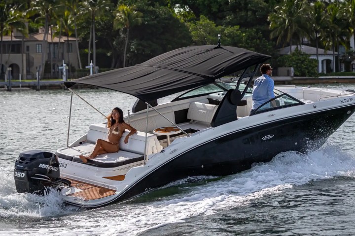 Man and woman enjoying a ride on a sleek black motorboat with a canopy on a sunny day.