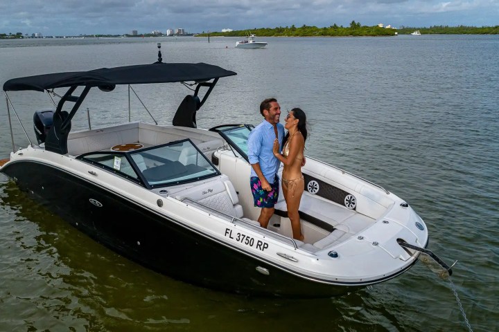 Couple enjoying on a motorboat in calm waters, with shoreline in the background.