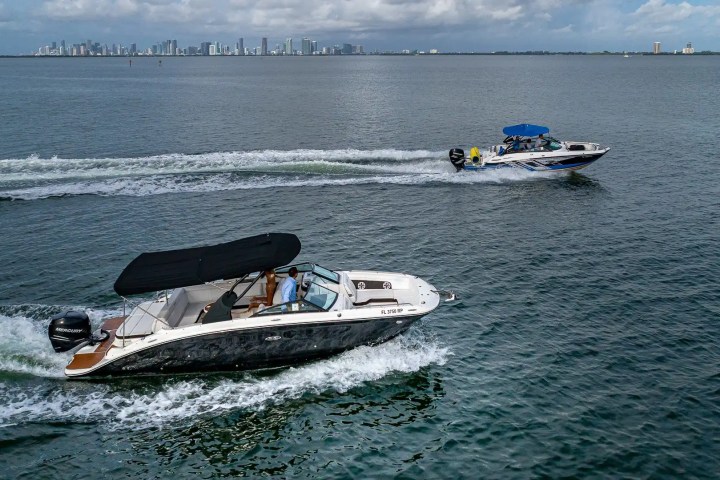 Two motorboats on a lake with a city skyline in the background under a cloudy sky.