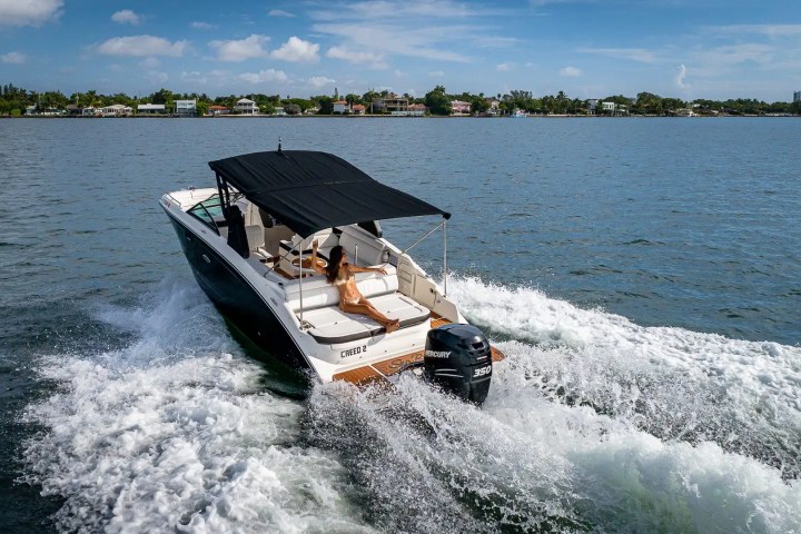 Speedboat with black canopy cruising on a scenic lake with a person reclining onboard.
