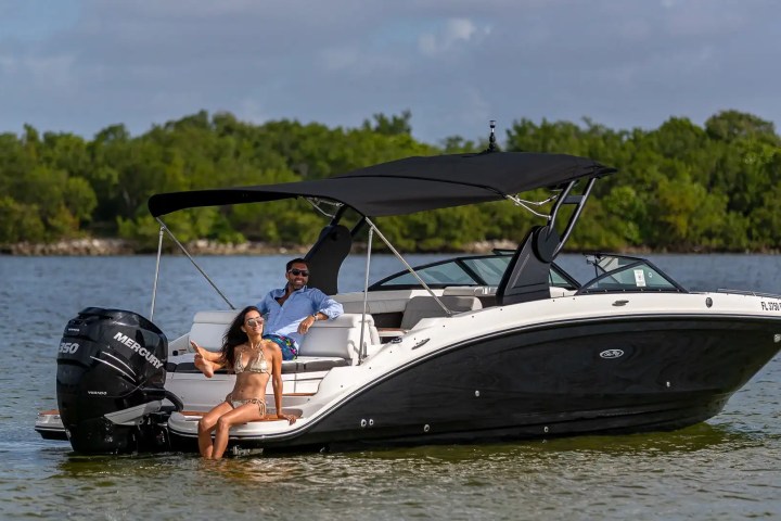 Two people relaxing on a motorboat with a canopy, floating on a calm lake.