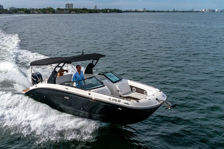 A black motorboat with people onboard cruising through water near a city shoreline.