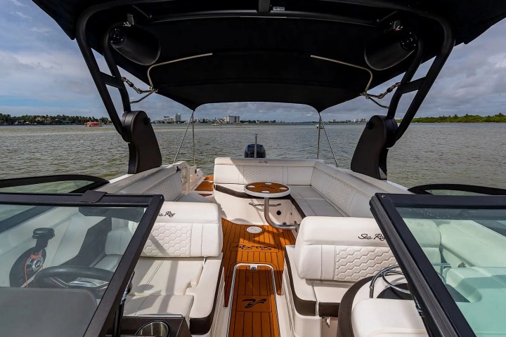 Interior view of a boat with seating and a small table, water and cityscape in the background.