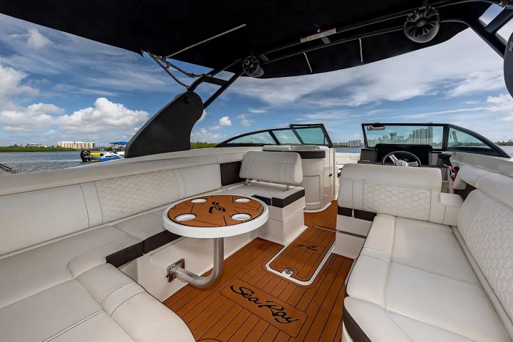Interior of a luxury boat with white seating and wooden deck under a blue sky.