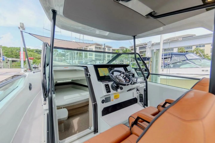Boat cockpit with leather seats, steering wheel, and electronic display, dockside view.