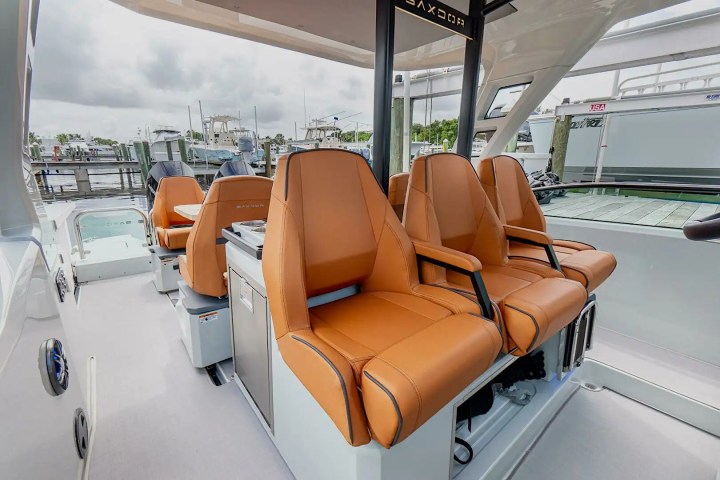 Four orange leather seats on a boat, overlooking a marina with cloudy skies.