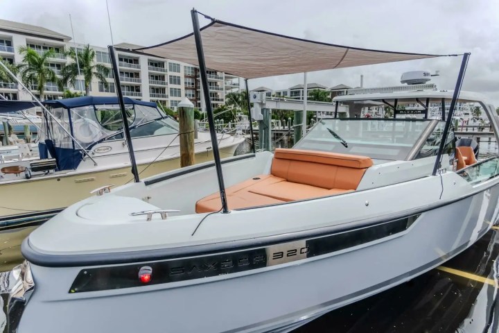 White boat with tan seats and canopy docked at marina with buildings in background.