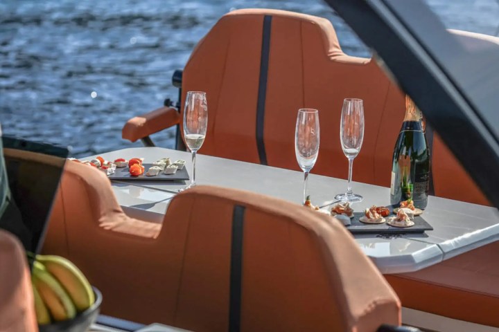 Boat interior with orange seats, table with appetizers, champagne bottle, and glasses by the water.