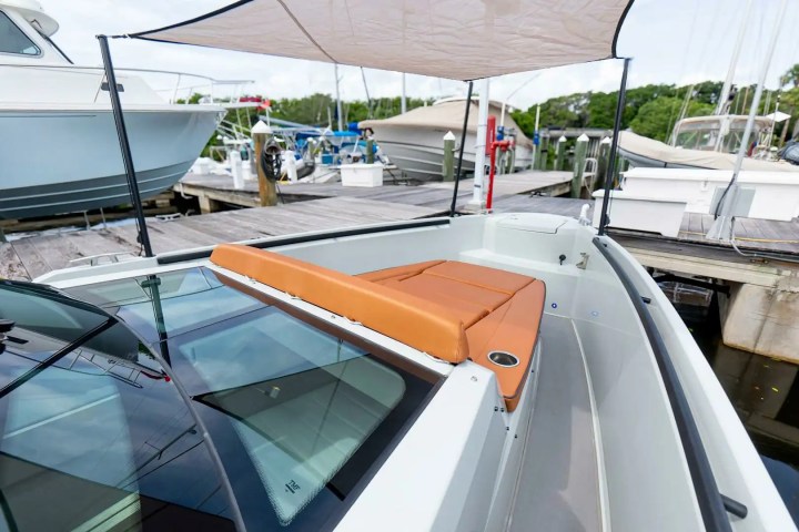 Boat with tan seats and canopy docked at marina, surrounded by other boats and wooden dock.