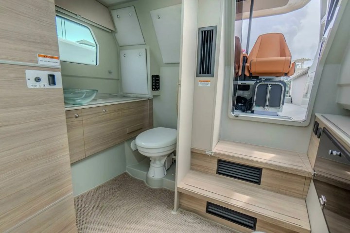 Compact boat bathroom with a toilet, glass sink, mirror, and wooden cabinets. Steps lead to an outdoor area.