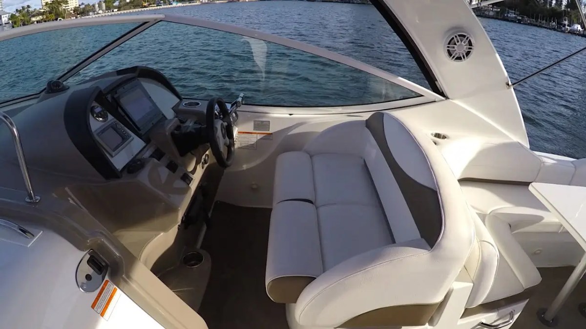 Interior of a boat cockpit with a steering wheel, controls, and white seating.