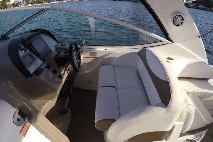 Interior of a boat cockpit with a steering wheel, controls, and white seating.