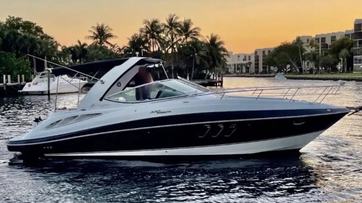 A motorboat on the water at sunset with trees and buildings in the background.