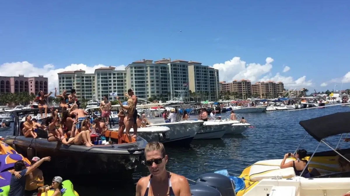 Crowd on boats enjoying sunny day near waterfront buildings and clear sky.