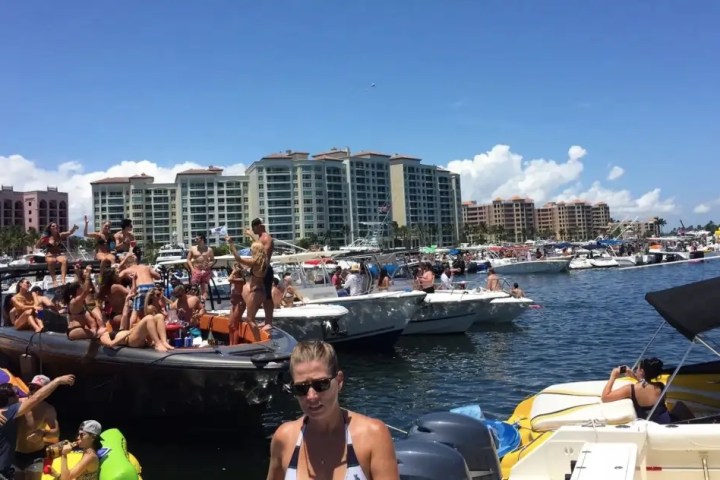 Crowd on boats enjoying sunny day near waterfront buildings and clear sky.