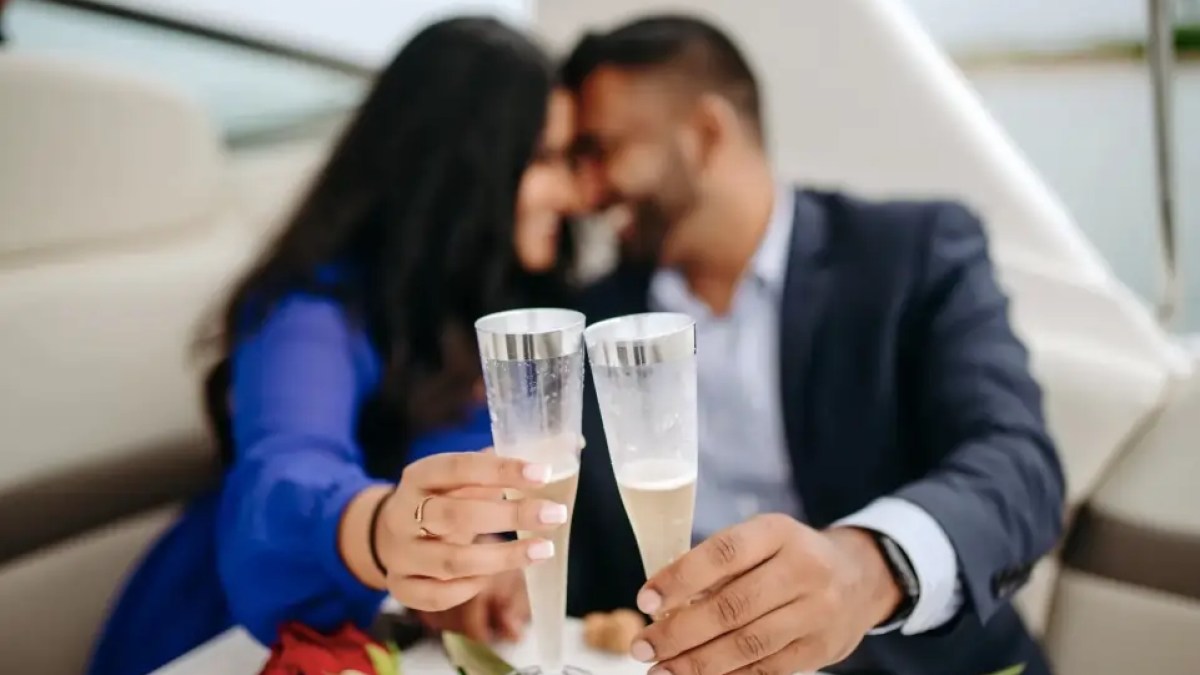 Couple toasting with champagne glasses, blurred faces, on a boat with a rose on the table.