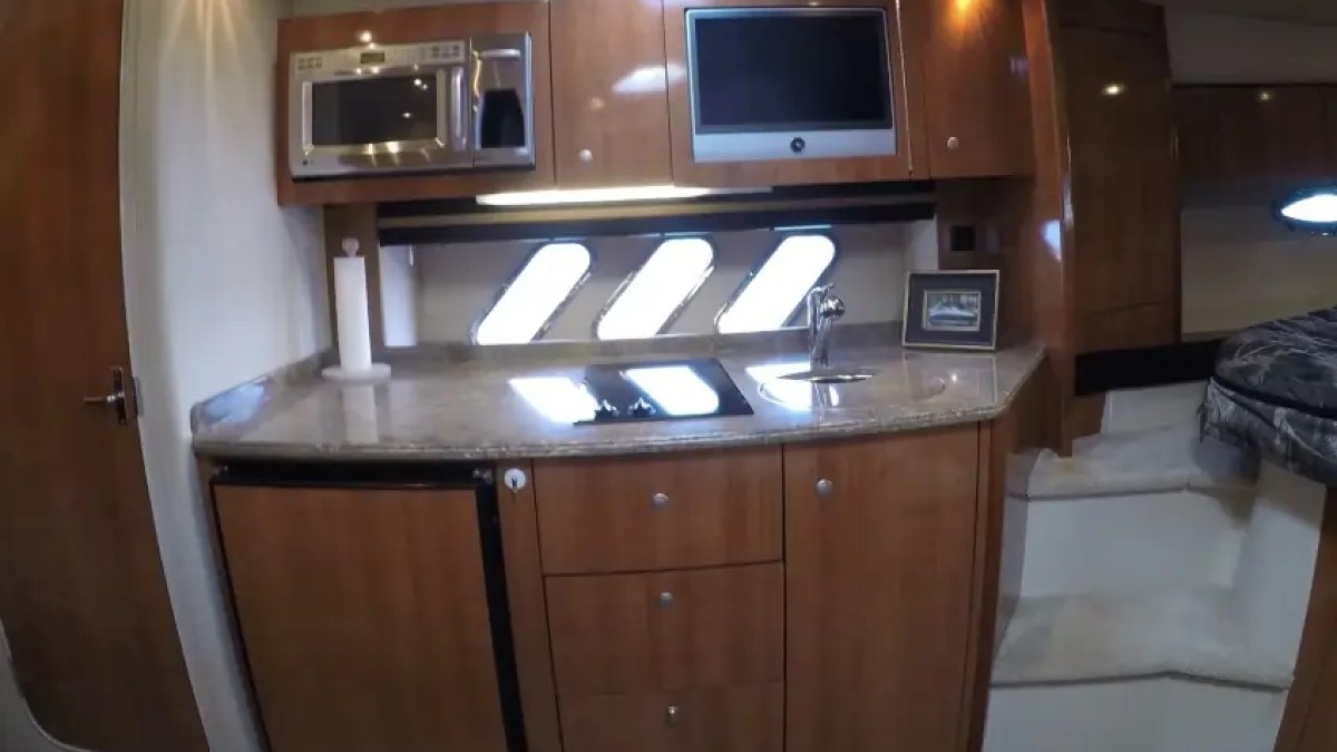 Interior of a yacht with wooden cabinets, microwave, sink, and small fridge.