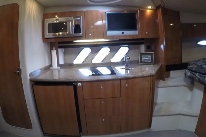Interior of a yacht with wooden cabinets, microwave, sink, and small fridge.