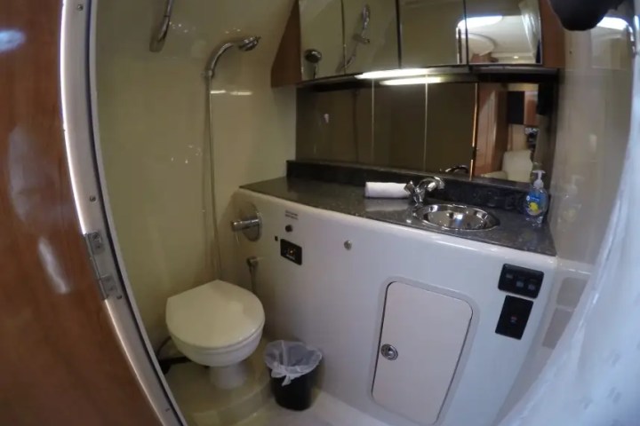Compact RV bathroom with toilet, sink, shower, and mirrored cabinets.