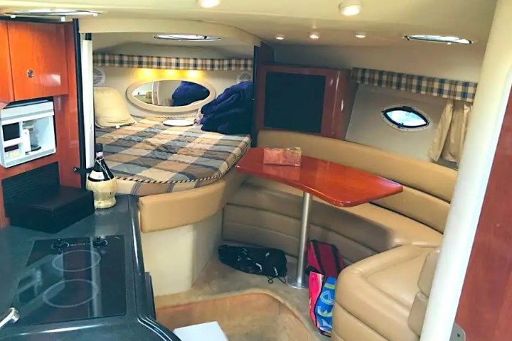 Cozy boat cabin with bed, kitchenette, and seating area with a table.